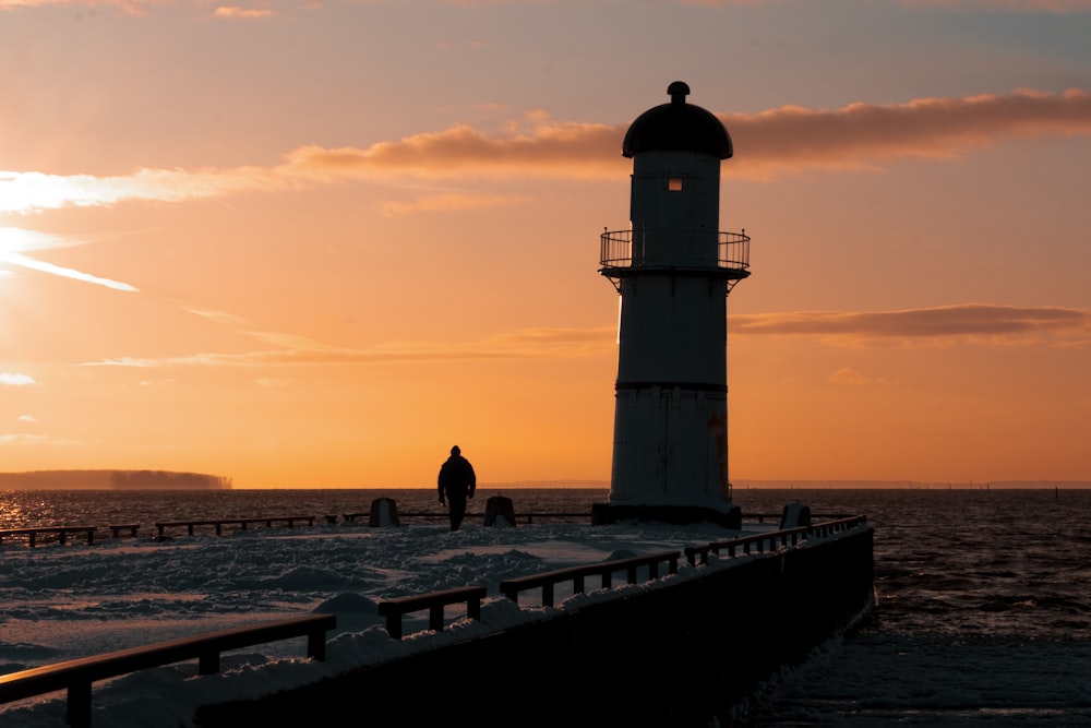 a person standing next to a lighthouse at sunset