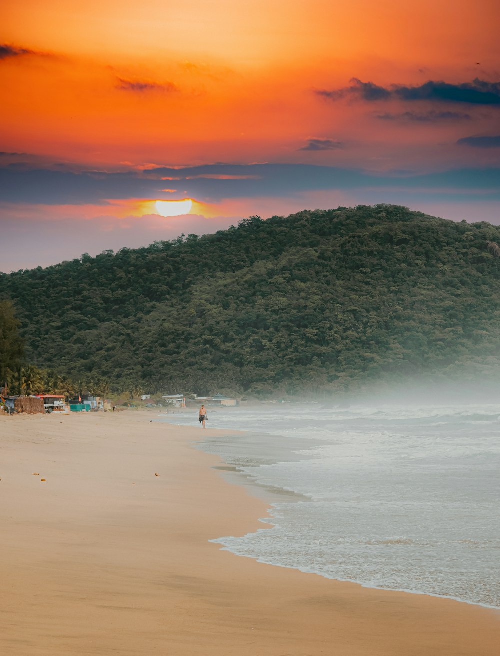 the sun is setting over a beach with a mountain in the background