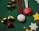 Festive decorations are arranged on a green textured surface. The items include red and white ornaments with 'JOY to the world' embroidered alongside a Christmas tree design, shiny golden and red bells, small wrapped gift boxes, and cut-out stars in silver and gold. Red and white tinsel strings accompany the ornaments, adding a cheerful and celebratory touch.