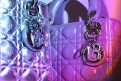 Two luxurious handbags with textured, quilted patterns are adorned with shiny metal charms. The lighting casts shades of purple and pink, creating a vibrant effect on the metallic surfaces.