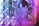 Two luxurious handbags with textured, quilted patterns are adorned with shiny metal charms. The lighting casts shades of purple and pink, creating a vibrant effect on the metallic surfaces.