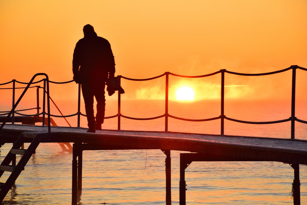 a man standing on a dock watching the sun go down