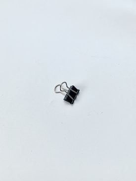 A single black binder clip lies on a smooth, white surface. The clip is metallic with two silver wire handles folded down.
