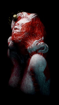 A surreal and abstract representation of a human form entangled in red thread-like structures. The figure appears to be crouching or kneeling with its face partially obscured. There is a prominent circular element resembling a clock or gear positioned above the head. The composition is set against a dark background, enhancing the contrast with the white and red colors.