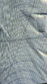 A textured fabric surface with a prominent crease running diagonally across it. The fabric displays a subtle, interwoven pattern with a mix of straight and curved lines. Lighting effects highlight the fabric's structure, creating a sense of depth and movement.