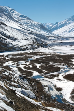 A panoramic view of Uttarakhand’s rugged mountains under a clear blue sky, with a winding river below
