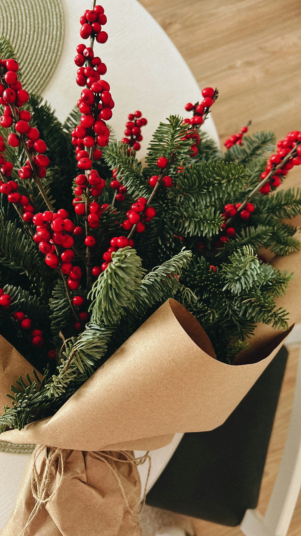 a bouquet of red berries and greenery wrapped in brown paper