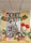 A festive Christmas display in an office setting featuring a decorated Christmas tree with ornaments and a star on top. Below the tree, various brightly wrapped gifts are arranged on a table. The backdrop includes metallic streamers and a large Santa balloon decoration. Above the tree, red and green balloons spell out 'MERRY CHRISTMAS'. Additional balloons with festive designs are placed around the setup, contributing to the cheerful atmosphere.