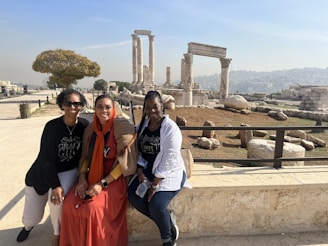 A group photo of smiling travelers posing in front of a historic landmark on a sunny day.