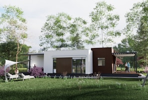 A modern, single-story house situated in a lush green garden with several trees surrounding it. The house has a combination of white and brown exterior walls, large windows, and a small patio area with people socializing. There are two lounge chairs positioned on a stretch of grass covered with a white canopy.