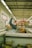 A person is lying on a freezer in a grocery store aisle, with one leg raised. They are holding a bag of snacks close to their face in a playful manner. The store interior is visible, with signs and shelves stocked with various products.