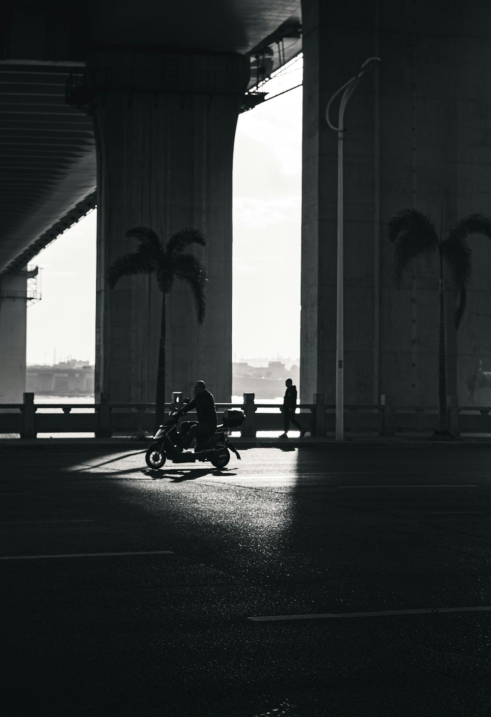 a man riding a motorcycle down a street under a bridge