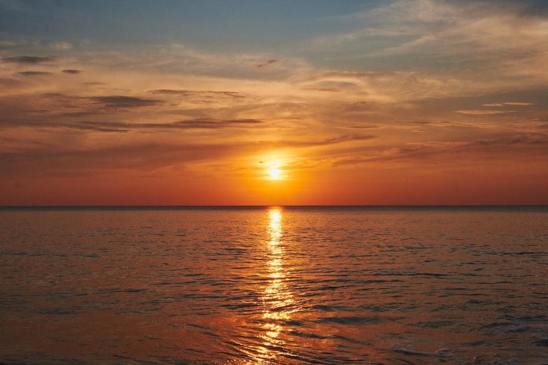 the sun is setting over the ocean on a cloudy day,
