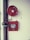 A fire safety setup featuring a red fire hose reel mounted on a wall alongside a rectangular red metal cabinet containing a fire hose and nozzle. Pipes and a valve are visible, highlighting the system's functionality.