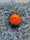 A single bright orange sits on a textured, dark granite surface. The surface has a speckled pattern with shades of black, gray, and white, creating a strong contrast with the vibrant orange.