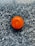 A single bright orange sits on a textured, dark granite surface. The surface has a speckled pattern with shades of black, gray, and white, creating a strong contrast with the vibrant orange.