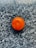 A single bright orange sits on a textured, dark granite surface. The surface has a speckled pattern with shades of black, gray, and white, creating a strong contrast with the vibrant orange.