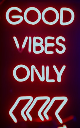 Bright neon sign with the phrase 'GOOD VIBES ONLY' glowing in white against a vibrant red background with four angled arrows underneath.