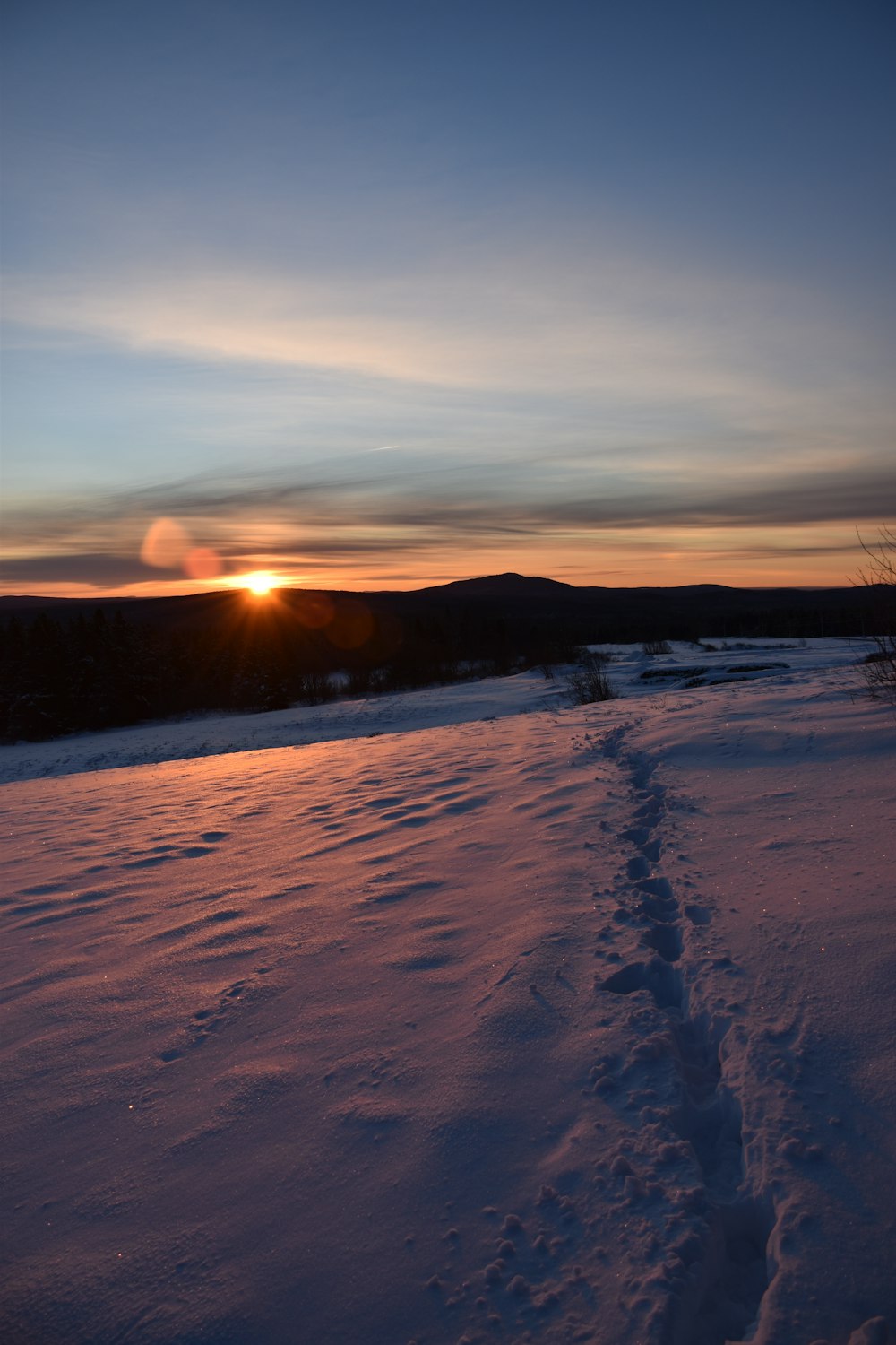 the sun is setting over a snowy field