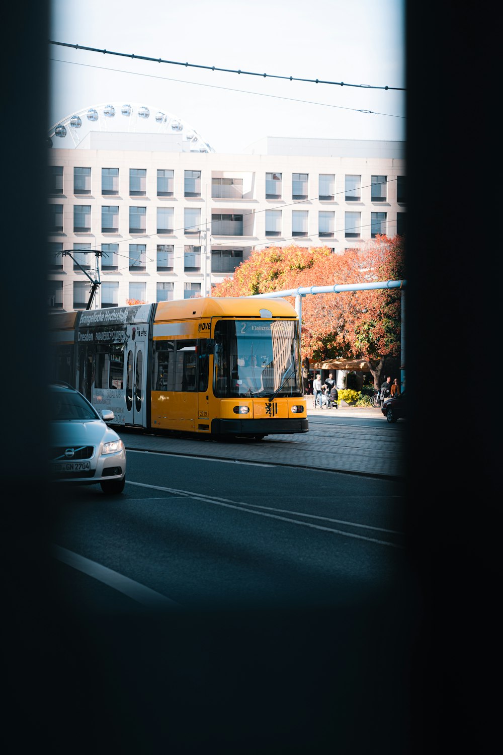 a yellow bus driving down a street next to a tall building