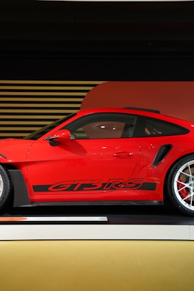 A sleek red Porsche 911 GT3 positioned on the right side against a blurred black gradient background.
