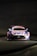 A race car is prominently displayed against a dark background. The vehicle is primarily pink, blue, and white, featuring branding from 'BWT' and 'AUTOHERO' on the hood and windshield. The car has a distinctive aerodynamic design typical of racing cars, with a prominent front grille and sleek headlights. Mercedes-Benz and Michelin logos are also visible on the car.