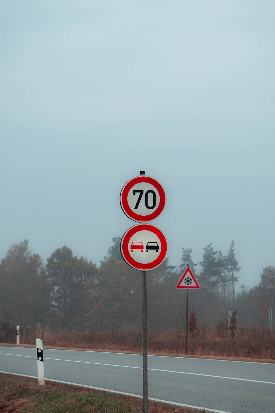 Two traffic signs mounted on a metal pole, one displays "70", the other has an