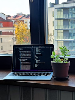 Close-up of a student coding an AI project on a laptop with German landmarks visible through the window.