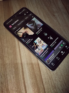 A smartphone is lying on a wooden surface, displaying a music streaming app that shows playlists and songs on the screen.