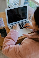 A person typing content on a laptop surrounded by digital accessories in pink and blue tones.