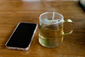 A sleek phone case in soft lavender resting beside a cup of tea on a minimalist wooden table.