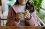 Close-up of a hand holding a warm cup of tea against a pink background
