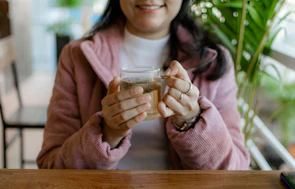 Close-up of a hand holding a warm cup of tea against a pink background