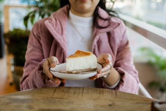A cheerful person enjoying a slice of Albina Cheesecake in a cozy kitchen setting.