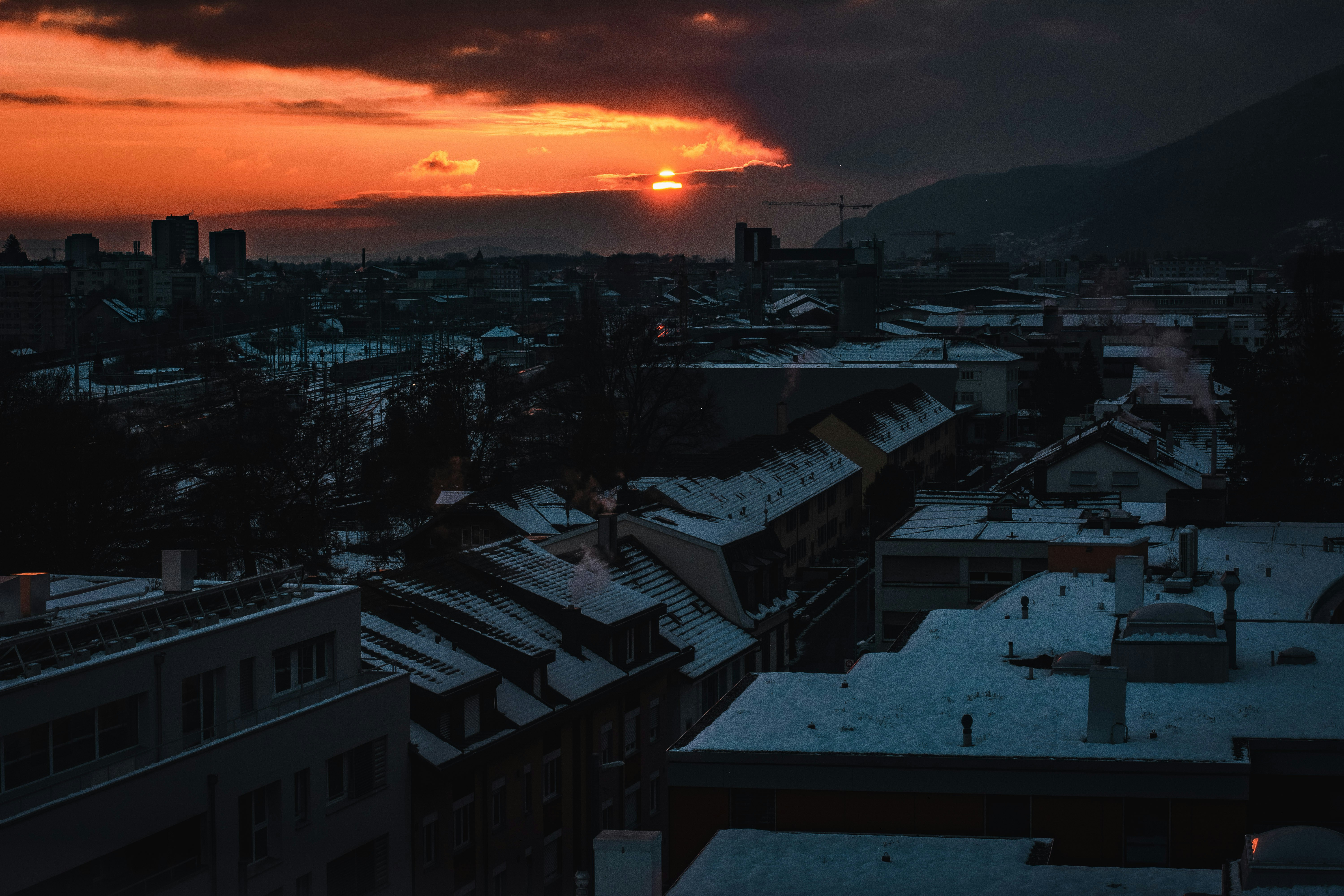the sun is setting over a city with snow on the roofs