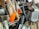 A collection of kitchen utensils and tools is densely packed, including a grater, knife sharpener, wooden spoon, and silicone brush. The utensils are made of metal, plastic, and wood, with some items overlapping each other.
