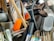 A collection of kitchen utensils and tools is densely packed, including a grater, knife sharpener, wooden spoon, and silicone brush. The utensils are made of metal, plastic, and wood, with some items overlapping each other.