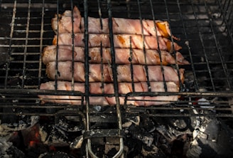 Crispy bacon strips crackling on the grill with glowing embers beneath