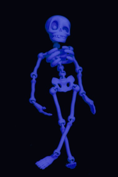 A cartoonish skeleton depicted in a glowing blue hue against a dark background. It has exaggerated, comical features with a large skull and oversized eye sockets, giving it a playful appearance.
