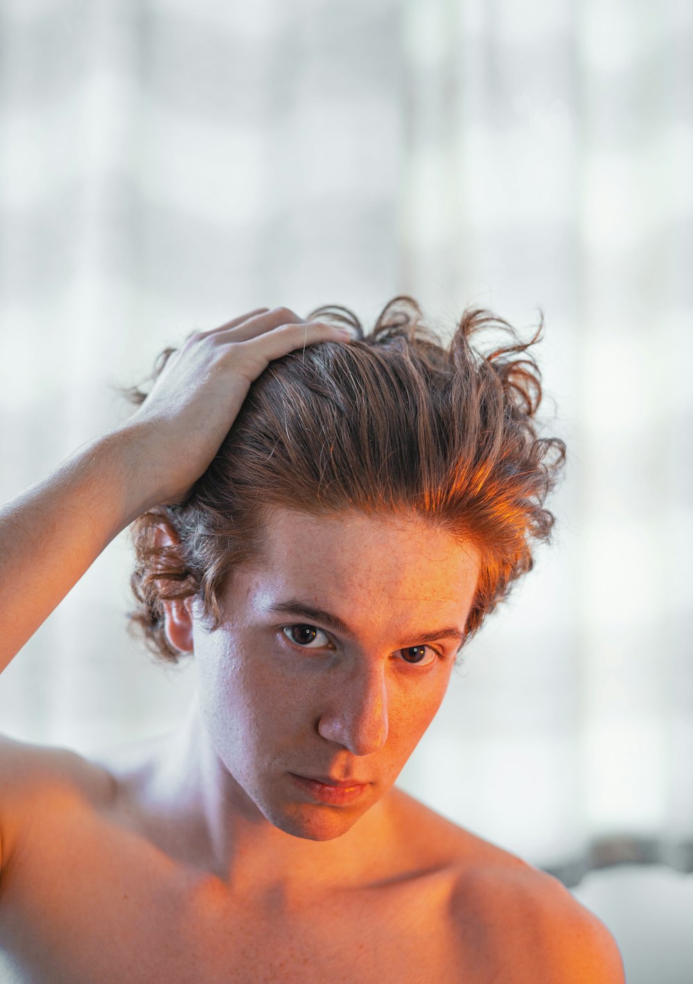 a shirtless man holding his hair in front of his face