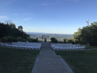 A serene lakeside setup with white chairs and floral arches under a clear blue sky.