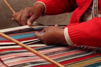 a woman weaving a rug with a wooden stick