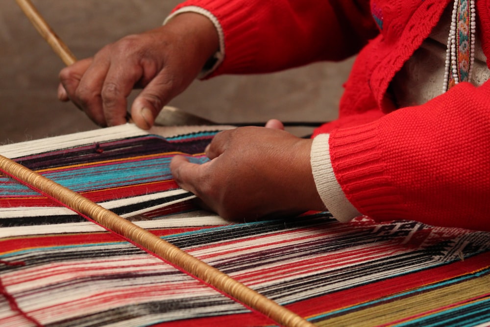 a woman weaving a rug with a wooden stick