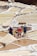 Several people are working in terraced salt pans, surrounded by piles of salt. They are wearing hats and boots, and one person is carrying a yellow container.