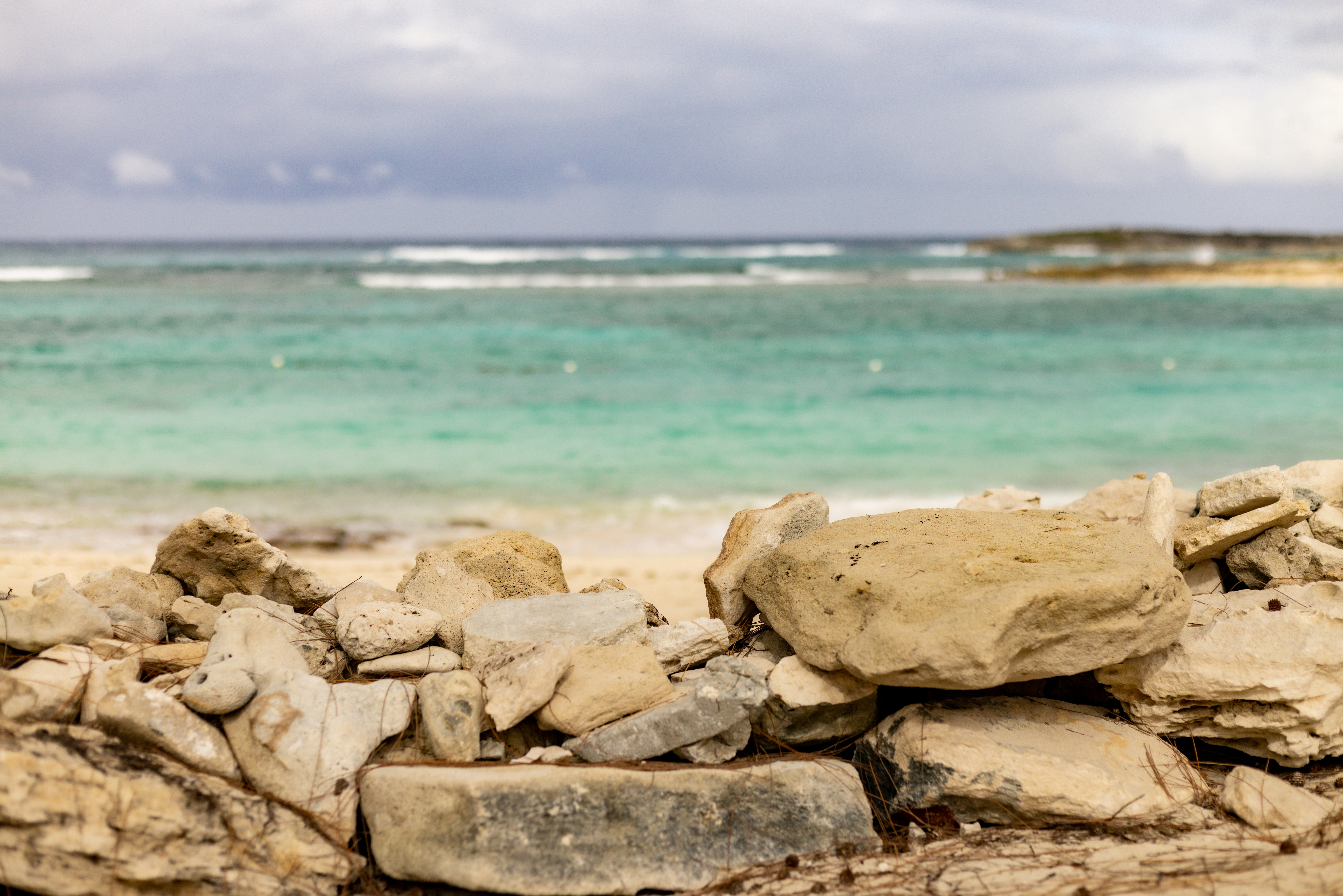 a pile of rocks sitting on top of a sandy beach, Rocky Bahamian beach! Blue ocean water in front of rocks