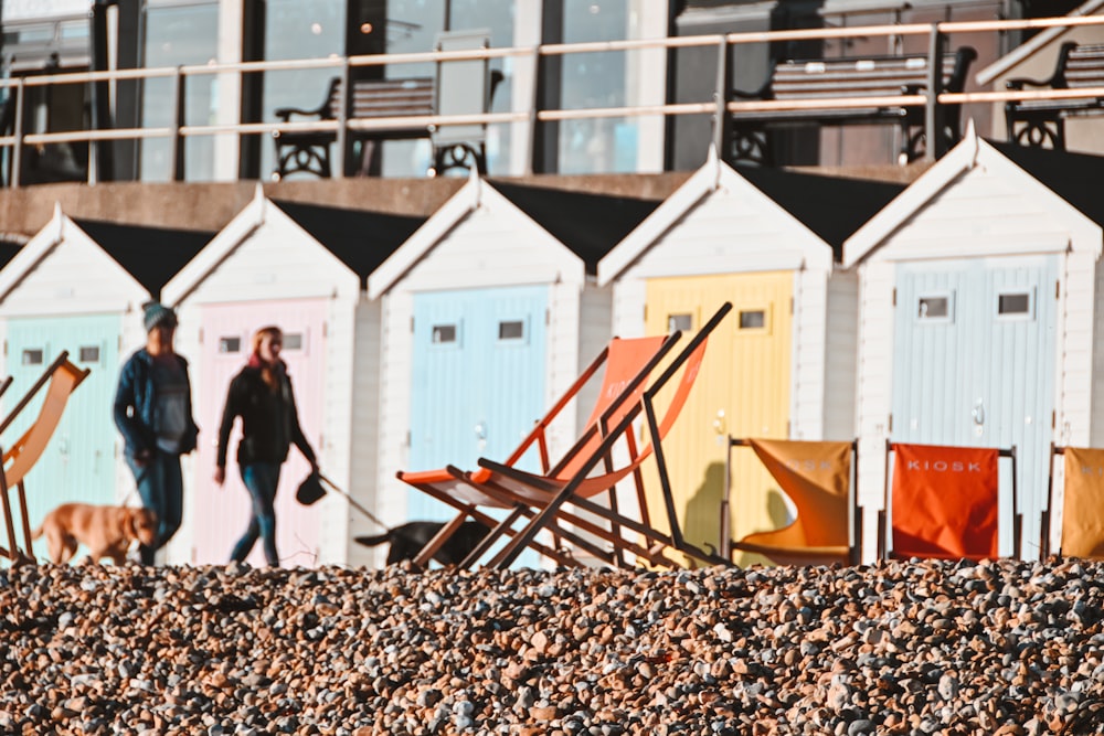 a woman walking a dog past a row of beach huts