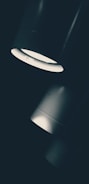 Three cylindrical lights are arranged diagonally, with a bright, focused beam shining downward. The lighting creates a dramatic contrast between the light and dark areas, emphasizing the sleek design of the fixtures.