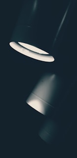 Three cylindrical lights are arranged diagonally, with a bright, focused beam shining downward. The lighting creates a dramatic contrast between the light and dark areas, emphasizing the sleek design of the fixtures.