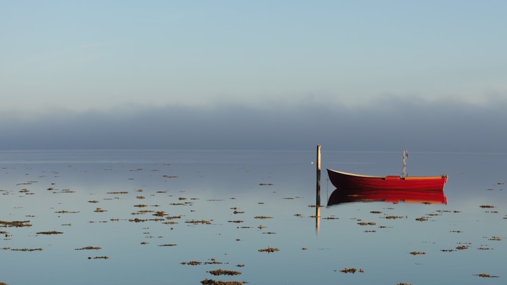 a red boat floating on top of a body of water