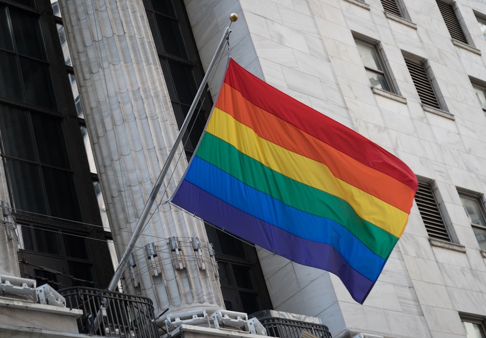 a rainbow flag flying in front of a tall building